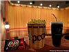 Candy, popcorn and soda placed on a ledge in front of a movie screen. 