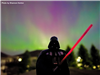 A toy figure of Darth Vader shown in the foreground with the Northern Lights in the background. 