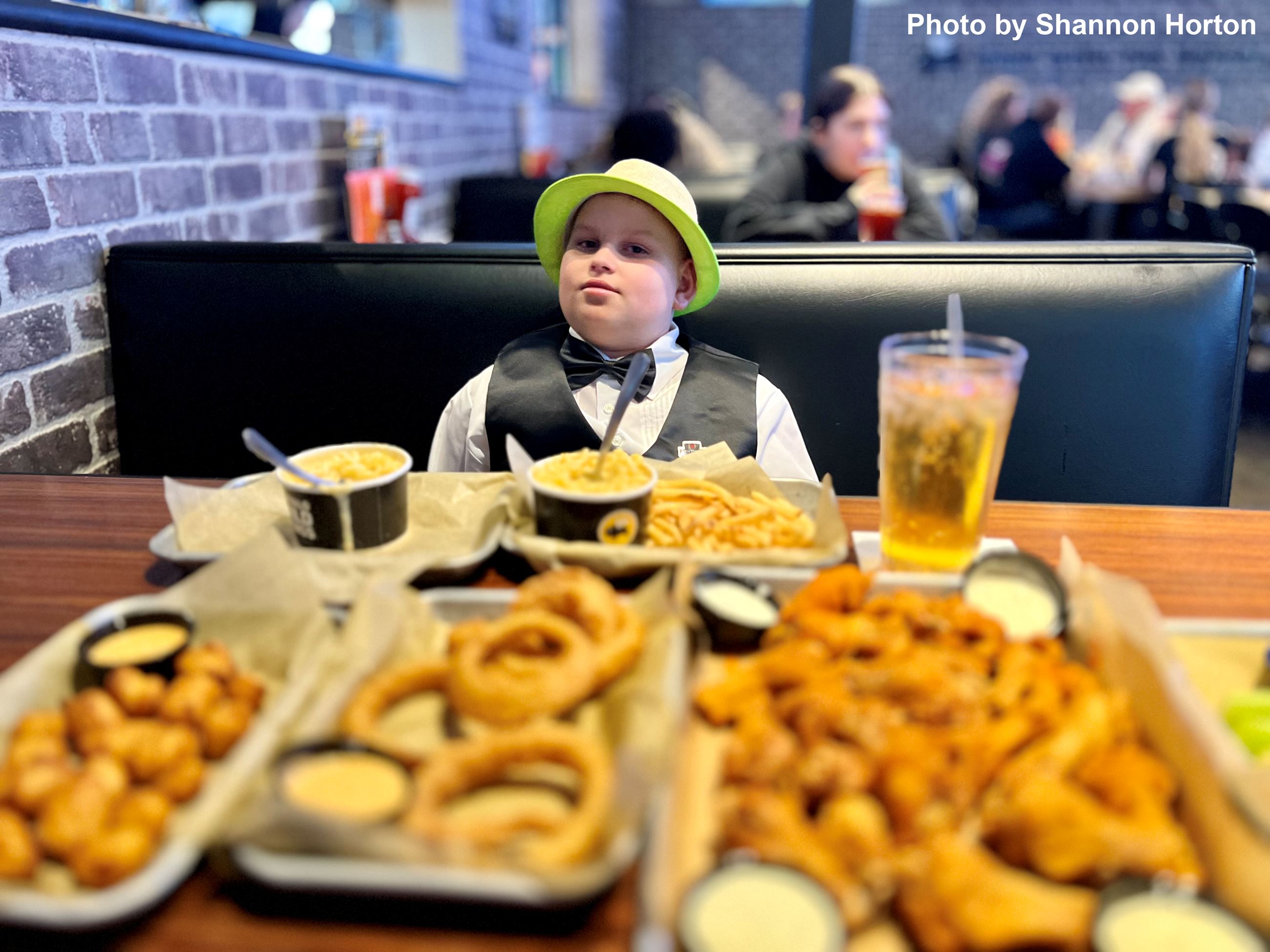 A boy seated at a restaurant with a variety of food on the table. 