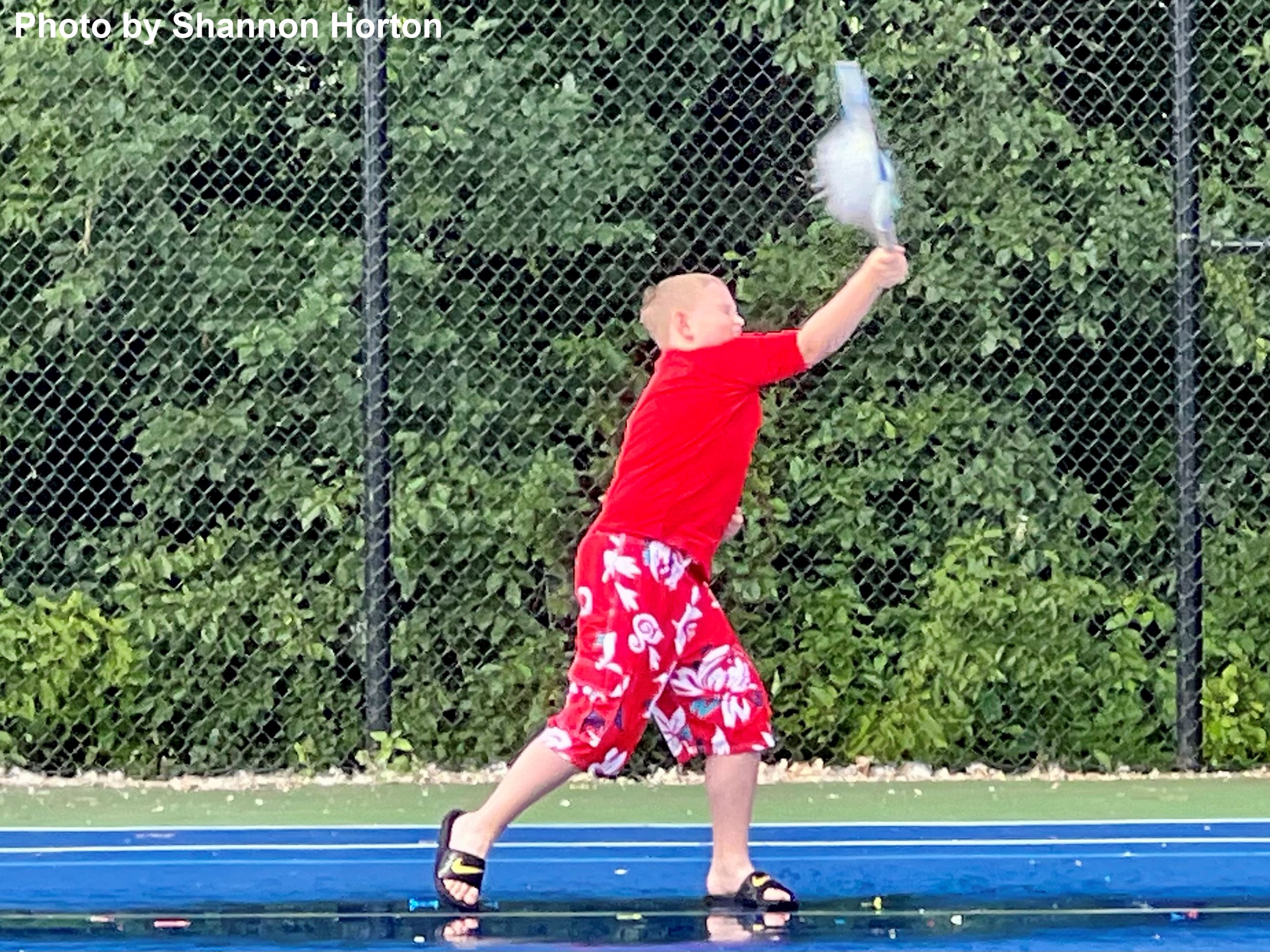 A boy playing tennis on a rainy court. 