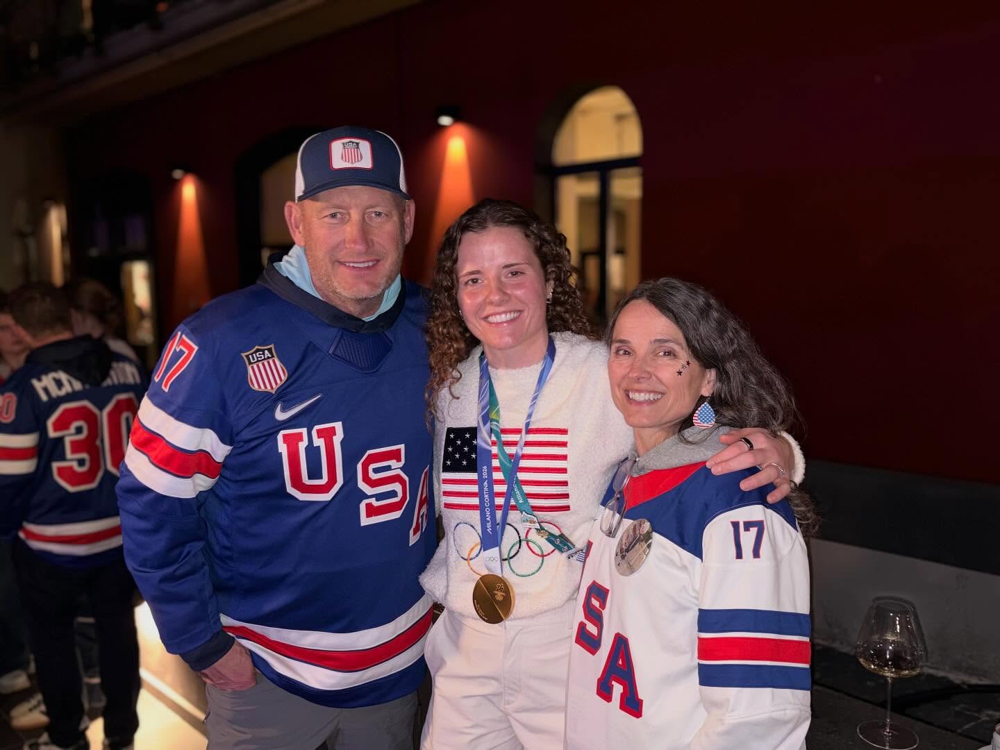 A man and woman standing with their daughter wearing a gold medal.