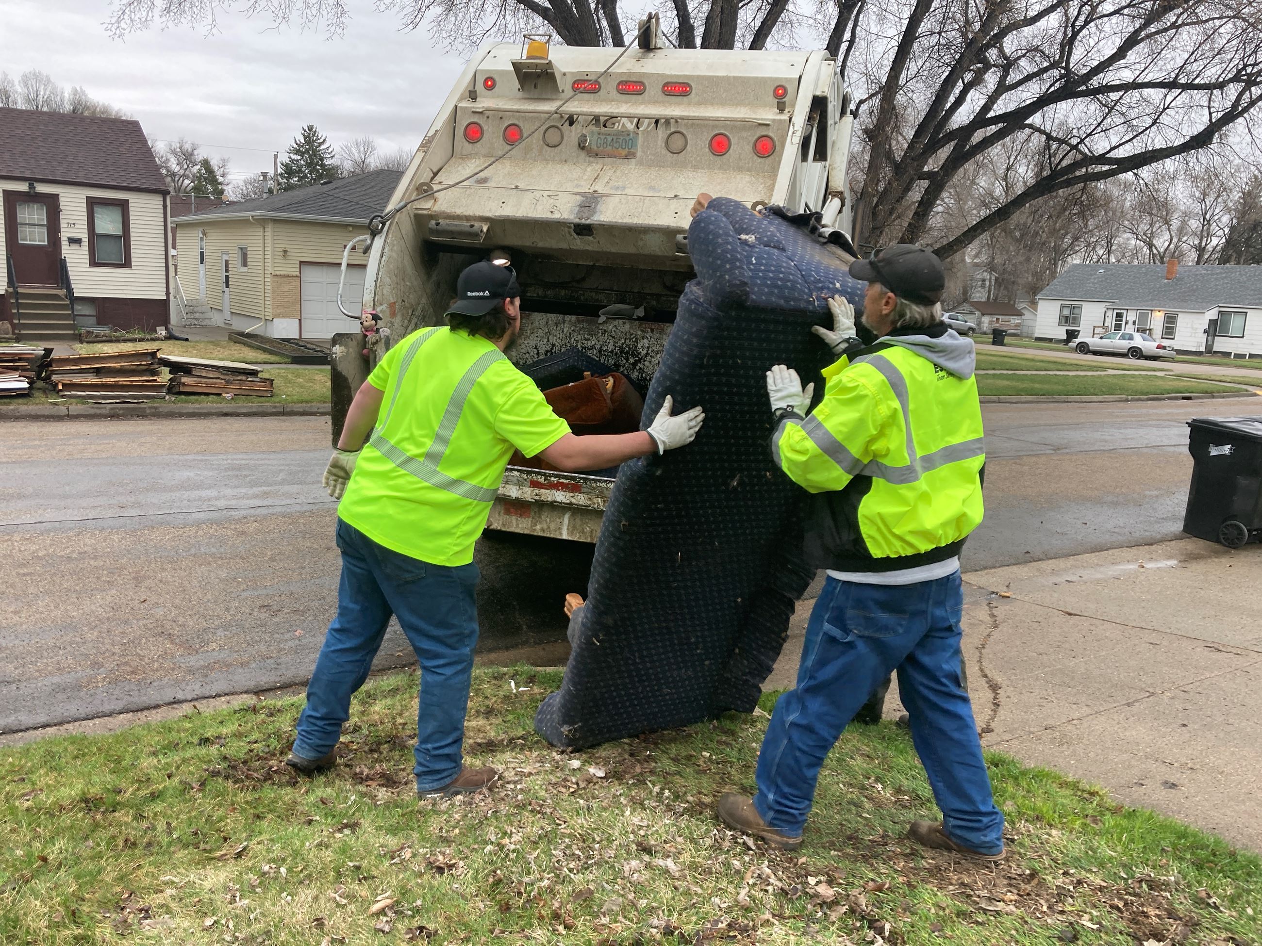 Public Works staff load a couch into a garbage truck. 